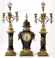 XX. sz. eleje: Nagyméretű neobarokk gyertyatartó pár és kandallóóra szett. Festett porcelán, réz. Óra szerkezete hiányos, számlapfa festett porcelán, hibátlan. Gyertyatartó: 70 cm, Óra: 55 cm.